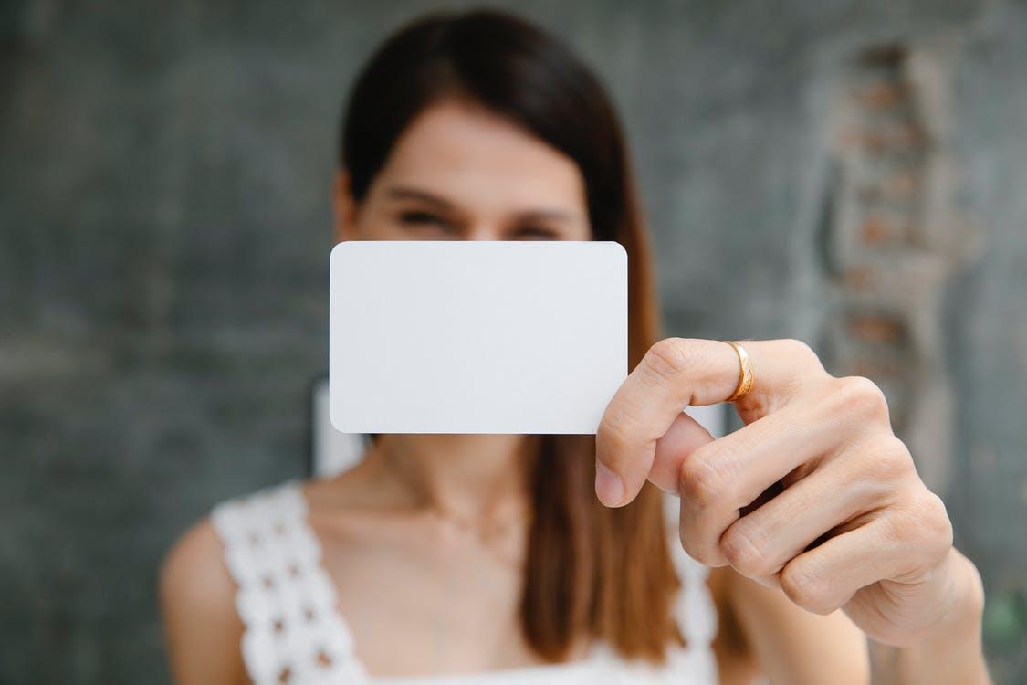 Free Young blurred female showing white blank business card and looking at camera in light room Stock Photo