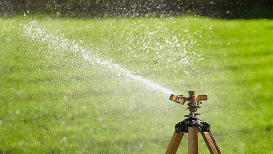 A tripod with an impact sprinkler spraying water in a garden