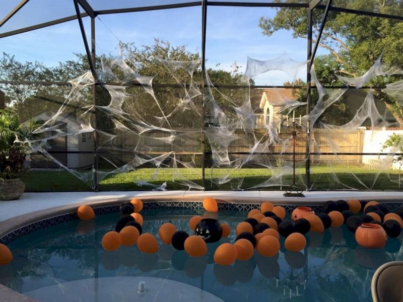 A pool with spider web decorations and orange & black balloons