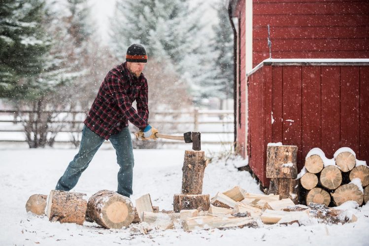 A man chopping wood with an axe in the snow