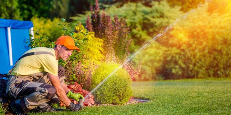 A man watering his lawn with a hose, searching for the best sprinkler