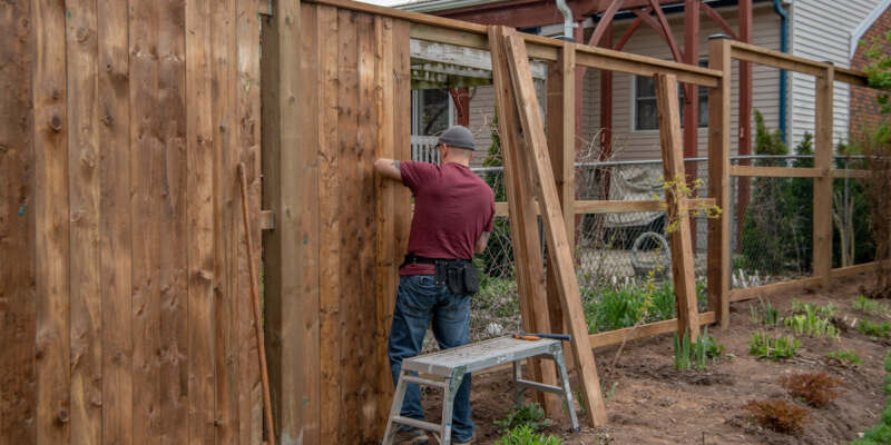 A man diligently constructing a wooden fence, showcasing his craftsmanship and dedication