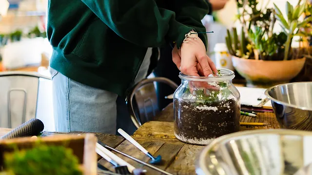 A person carefully arranging plants in a jar.